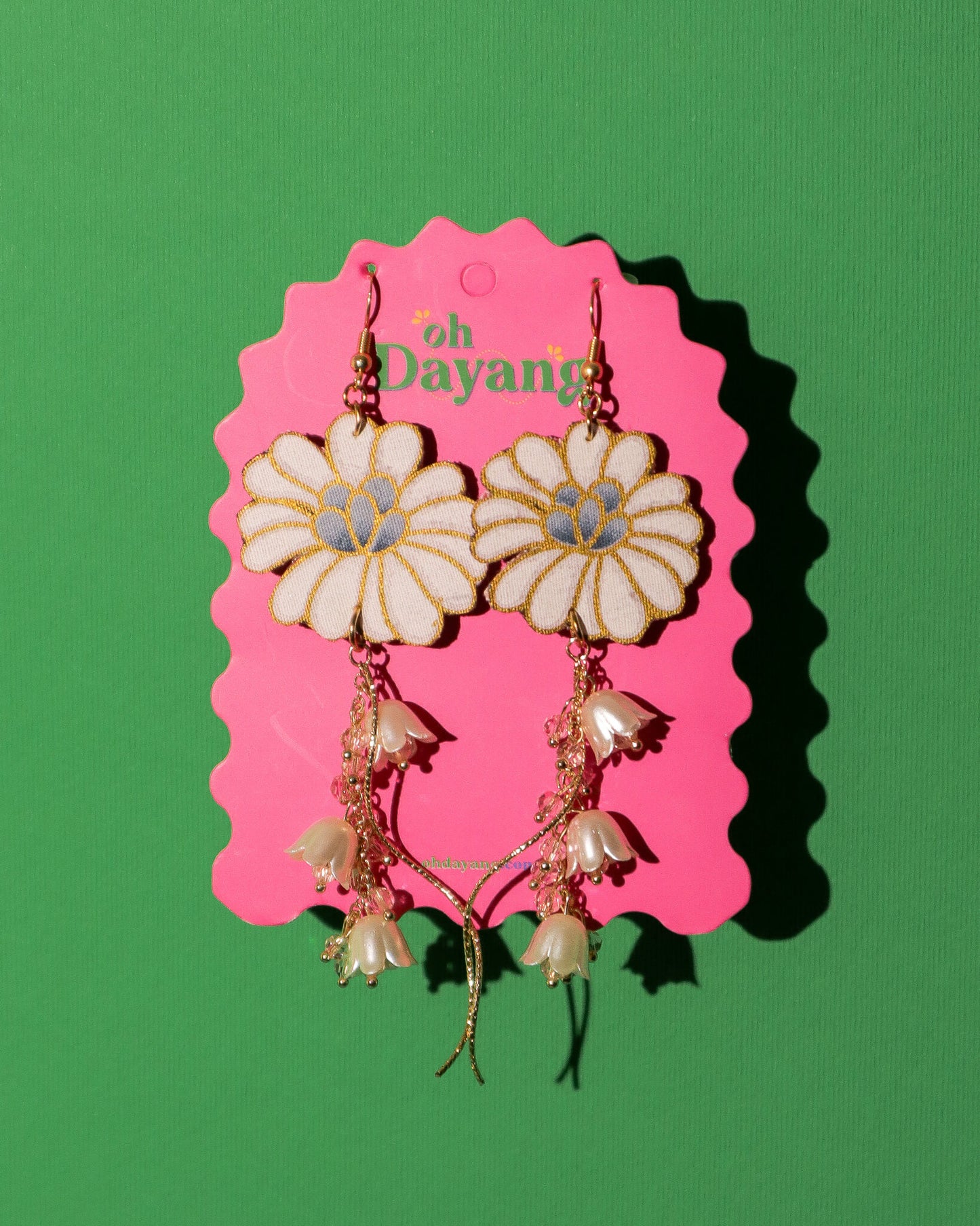 Floral earrings on a pink Dayang branded card against a green background